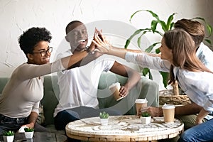 Happy diverse friends giving high five together in cafe