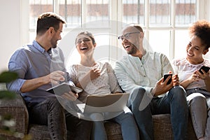 Happy diverse friends laughing at funny joke, using electronic devices