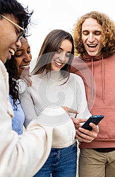 Happy diverse friends laughing while watching funny videos on smartphone