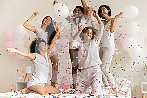 Happy diverse girls wearing pajamas throwing confetti, having fun