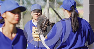 Happy diverse group of female baseball players smiling and banging gloves after game