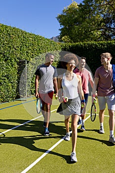 Happy diverse group of friends arriving together at tennis court