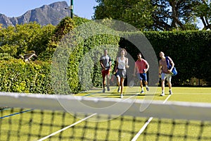 Happy diverse group of friends arriving together at tennis court