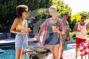 Happy diverse group of friends having pool party, barbecuing together in garden