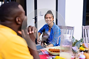 Happy diverse group of friends playing guitar and having dinner