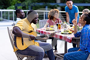 Happy diverse group of friends playing guitar and having dinner