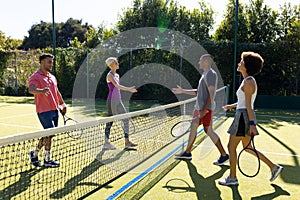 Happy diverse group of friends playing tennis, shaking hands at tennis court