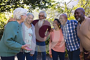 Happy diverse group of senior friends embracing and laughing in sunny garden