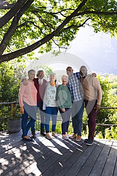 Happy diverse group of senior friends embracing and smiling in sunny garden