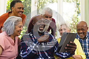 Happy diverse group of senior friends having video call and laughing in sunny living room