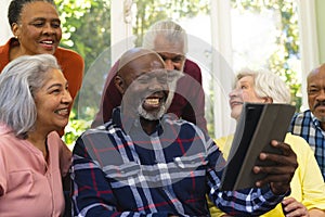 Happy diverse group of senior friends having video call and laughing in sunny living room