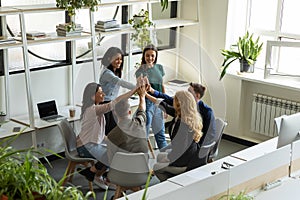 Happy diverse interns with female leader, coach giving high five.