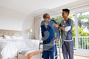 Happy diverse male doctor helping senior male patient using crutches at home