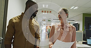 Happy diverse male and female business colleagues talking and walking in office