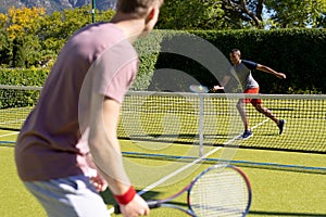 Happy diverse male friends playing tennis together at tennis court