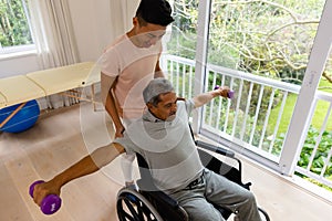 Happy diverse male physiotherapist advising and senior male patient in wheelchair using dumbbells