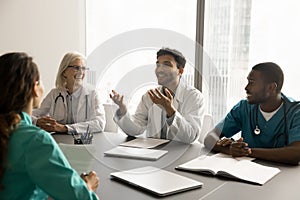 Happy diverse medical team of colleagues talking at meeting table