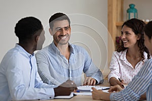 Happy diverse millennial employees talking at meeting table