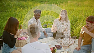 Happy Diverse Multiethnic Friends have picnic. Ukulele lesson in park