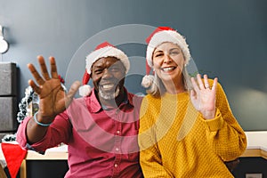 Happy diverse senior couple in santa hats making christmas video call waving to camera