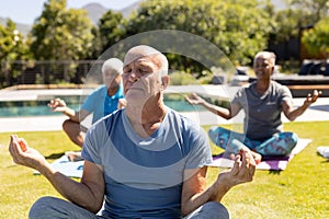 Happy diverse senior friends practicing yoga meditation sitting in sunny garden