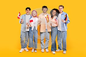 Happy diverse students of language school, teens of different nationalities holding little flags, yellow background