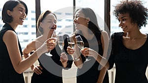 Happy diverse women wearing elegant black dresses clinking champagne glasses photo