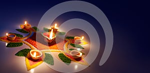 Diya oil lamps lit on colorful rangoli with copy space