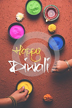 Happy Diwali Greeting card using colourful Rangoli in bowls, diya or clay lamp and happy diwali writing with flowers