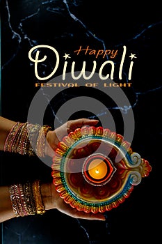 Happy Diwali - Woman hands with henna holding lit candle isolated on dark background