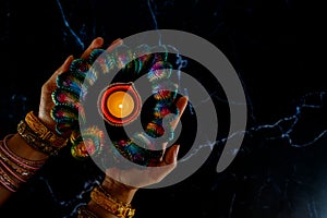 Happy Diwali - Woman hands with henna holding lit candle isolated on dark background