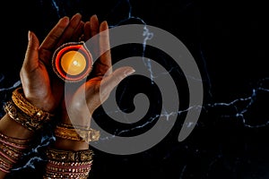 Happy Diwali - Woman hands with henna holding lit candle isolated on dark background