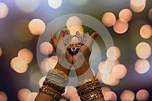 Happy Diwali - Woman hands with henna holding lit candle isolated on dark background. Clay Diya lamps lit during Diwali, Hindu