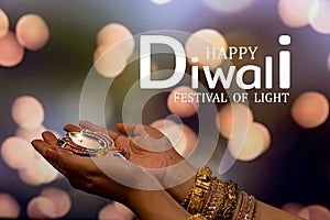 Happy Diwali - Woman hands with henna holding lit candle isolated on dark background. Clay Diya lamps lit during Dipavali, Hindu