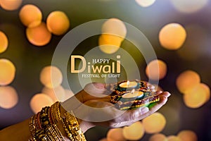 Happy Diwali - Woman hands with henna holding lit candle isolated on dark background. Clay Diya lamps lit during Dipavali, Hindu