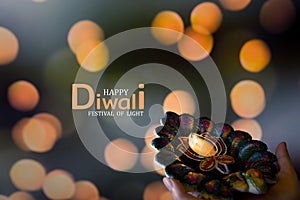 Happy Diwali - Woman hands with henna holding lit candle isolated on dark background. Clay Diya lamps lit during Dipavali, Hindu