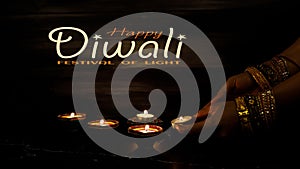 Happy Diwali - Woman hands with henna holding lit candle isolated on dark background