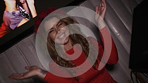 Happy dj girl in red dress with rim on head clap in hands at turntable in club.