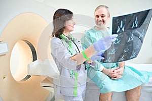 Happy doctor holding MRI images in clinic while talking with patient