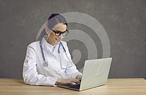 Happy doctor with laptop working online sitting at desk studio portrait shot