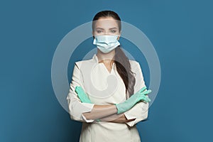 Happy doctor or nurse woman in protective medical mask and surgical gloves on blue background.  Medicine, assistance, safety and