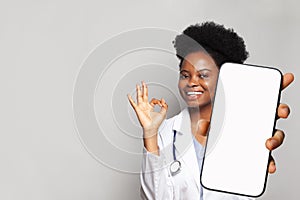 Happy doctor shows a phone with a blank display. Online medical consultation and medical healthcare and application