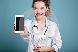 Happy doctor in white coat showing blank smartphone screen