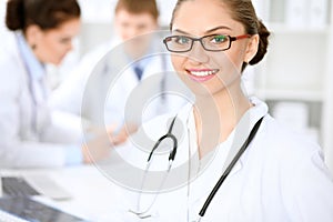 Happy doctor woman with medical staff at the hospital sitting at the table. Red frame glasses