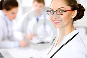 Happy doctor woman with medical staff at the hospital sitting at the table. Red frame glasses