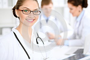 Happy doctor woman with medical staff at the hospital sitting at the table. Red frame glasses