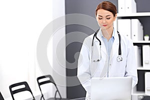 Happy doctor woman at work. Portrait of female physician using laptop computer while standing near reception desk at