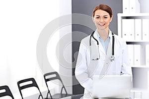 Happy doctor woman at work. Portrait of female physician using laptop computer while standing near reception desk at