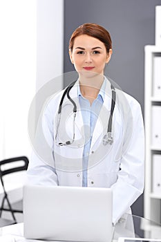 Happy doctor woman at work. Portrait of female physician using laptop computer while standing near reception desk at