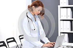 Happy doctor woman at work. Portrait of female physician using laptop computer while standing near reception desk at